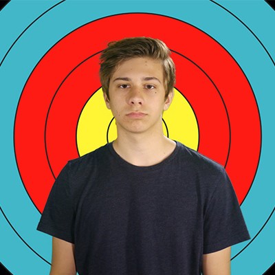 Glum teen boy with medium brown hair in front of an archery target